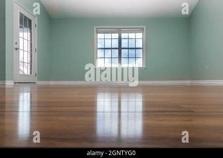 Una camera verde vuota con pavimenti in legno chiaro e una finestra Foto Stock