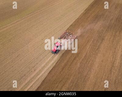 Foto aerea di un trattore che aratura un campo stoppia in campagna. Il trattore agricolo aratri terreno per la semina. Vista dall'alto dal drone . Foto Stock