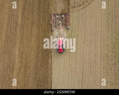 Foto aerea di un trattore che aratura un campo stoppia in campagna. Il trattore agricolo aratri terreno per la semina. Vista dall'alto dal drone . Foto Stock