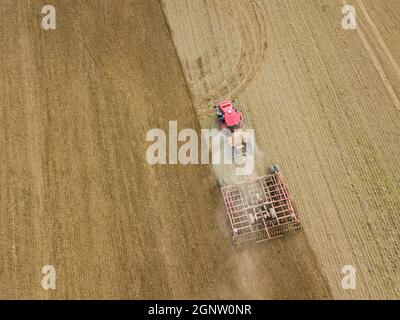 Foto aerea di un trattore che aratura un campo stoppia in campagna. Il trattore agricolo aratri terreno per la semina. Vista dall'alto dal drone . Foto Stock