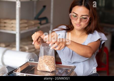 Mani donna focalizzate che confezionano grani in sacchetto trasparente da vendere. Lenticchie e deposito di grano. Foto Stock