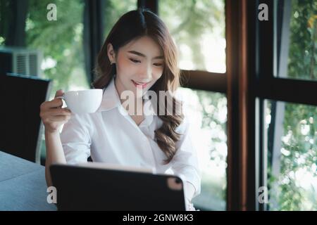 Immagine di bella donna di affari tiene una tazza di caffè e controlla il suo email prima di andare al lavoro Foto Stock