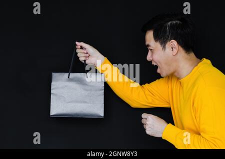 Asian Happy maschio che tiene borse shopping su sfondo scuro per Black Friday concetto. Foto Stock