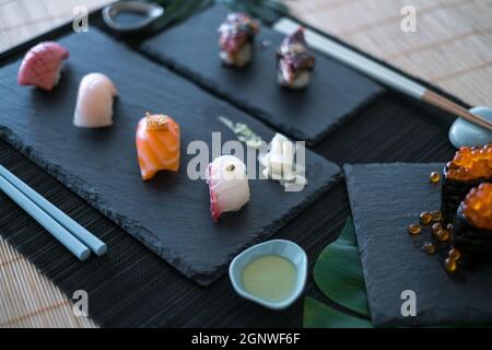 Cucina giapponese. Delizioso sushi con vari tipi di sushi nigiri con salmone, tonno, anguilla, caviale di salmone rosso servito su tavole di ardesia nera Foto Stock