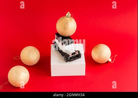 Modello di auto giocattolo retrò bianco su sfondo rosso e palle d'oro di Natale. Il concetto di vacanze di Capodanno, sconti e vendite Foto Stock