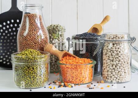 Assortimento di legumi colorati in vasetti e bicchieri su un tavolo da cucina leggero Foto Stock