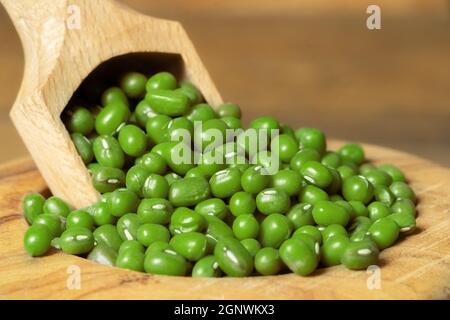 Primo piano di fagioli di soja in una ciotola con un cucchiaio. Piselli verdi secchi in una ciotola di legno su sfondo di legno. Foto Stock