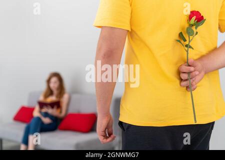 Il primo piano di un uomo nasconde una rosa dietro per fare una sorpresa al suo partner. Romanticismo, anniversario e concetto di regalo. . Foto di alta qualità Foto Stock