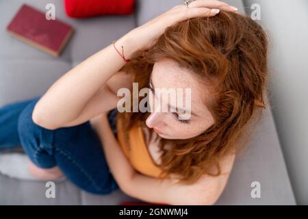 Triste giovane donna è seduta sul couach ha messo la sua mano sulla sua testa mentre lei pensa. . Foto di alta qualità Foto Stock