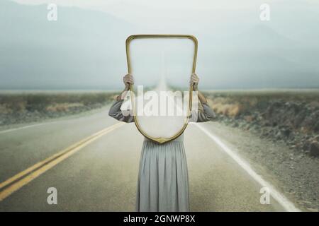 la donna si nasconde tenendo uno specchio davanti al suo volto; introspezione percorso concetto Foto Stock