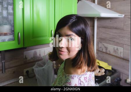 Bella giovane donna dai capelli neri con un sorriso sul viso, toglie i prodotti da un pacchetto, andando a cucinare la cena in una cucina con forno verde Foto Stock