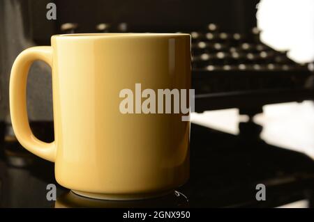 Un primo piano di un desktop scrittori con una profondità di campo poco profonda fuoco sulla tazza di caffè con area per copyspace e una macchina da scrivere blurry sullo sfondo Foto Stock
