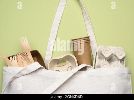 borsa in tessuto bianco e stoviglie monouso di carta da artigianato marrone su sfondo verde. Vista dall'alto, concetto di rifiuto della plastica, zero sprechi Foto Stock