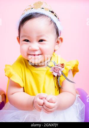 Primo piano faccia principessa bambina in bel vestito è sorriso in studio su sfondo rosa, Baby 9 mesi Foto Stock