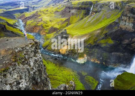 Donna escursionista che gode Highlands d'Islanda. Fiume Fossa nella valle del canyon Landmannalaugar. Colline e scogliere sono coperte da muschio verde Foto Stock