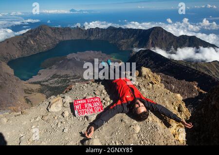 Un giovane uomo si trova sulla roccia in cima al Monte Rinjani, Lombok, Indonesia Foto Stock