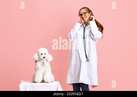 Ritratto concettuale di giovane bella donna, veterinario con cane da cuccioli bianco isolato su sfondo rosa studio. Cura del PET, animale nell'uomo Foto Stock