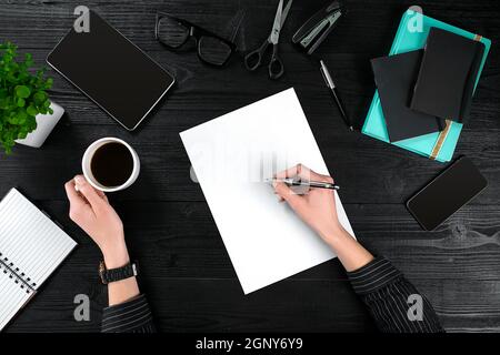 Scrivania donna d'affari con diversi oggetti. La mano di una donna scrive in un taccuino Foto Stock