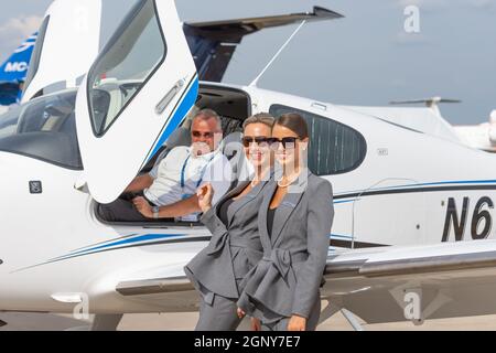 Sorridendo le ragazze in un vestito di affari e un pilota dell'aeroplano sullo sfondo di un aeroplano leggero-motore. Russia. Mosca. 21 luglio 2021 Foto Stock