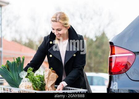 Donna che carica i generi alimentari dopo aver fatto acquisti nel tronco della sua auto sul posto di parcheggio Foto Stock