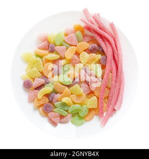 Caramelle gommosi sotto forma di fette di frutta, bastoncini di zucchero su un piatto, isolato su sfondo bianco. Vista dall'alto. Foto Stock