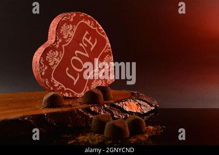 Una scatola rossa a forma di cuore e alcuni sottili tartufi di cioccolato sciolti. Foto Stock