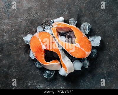 Due bistecche di salmone selvatico crudo su ghiaccio su sfondo nero testurizzato. Bistecche di salmone vista dall'alto o piatto. Foto Stock