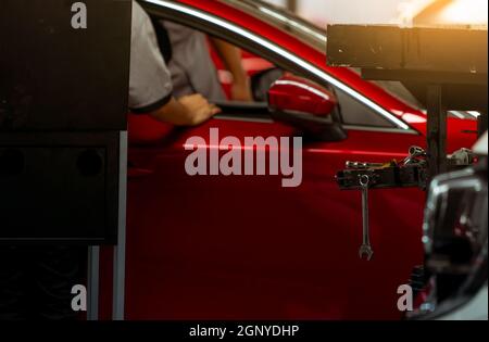 La chiave pende sulla rastrelliera attrezzi in officina su un tecnico meccanico sfocato e un'auto SUV rossa parcheggiata in officina di riparazione auto. Auto rossa in garage per la riparazione e principale Foto Stock