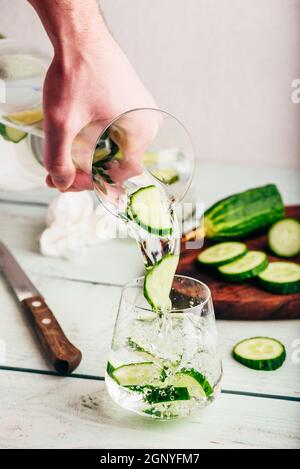 Mano con caraffa versa acqua detox con fette di cetriolo Foto Stock