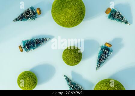 Sfondo concettuale di Natale e Capodanno con piccoli alberi di natale e palle verdi su sfondo blu. Ombre dure alla moda, scatto in studio Foto Stock
