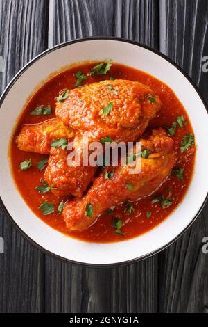 Ayam Masak Merah delizioso pollo fritto marinato con curcuma e fatto cuocere in un primo piano con sugo di pomodoro leggermente speziato in una ciotola sul tavolo. Vertica Foto Stock