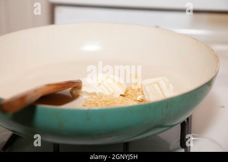 Aglio sminuzzato e burro in una padella con un cucchiaio per agitazione in legno Foto Stock