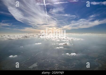 Vista aerea dalla finestra dell'aeroplano ad alta quota di città lontana coperta da strato di smog sottile e nubi distanti. Foto Stock