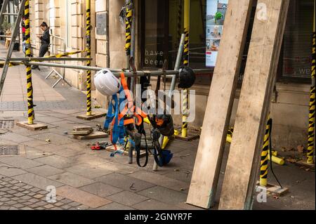 Ponteggi su un edificio con imbracature di sicurezza e cappelli duri appesi al ponteggio con alcuni pannelli di affare si alzarono contro il ponteggio Foto Stock