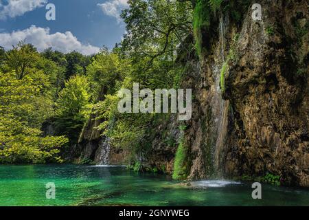Cascate che scendono da alte scogliere o rocce verso il lago di colore turchese nel Parco Nazionale dei Laghi di Plitvice, patrimonio dell'umanità dell'UNESCO, Croazia Foto Stock