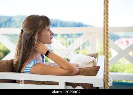 Giovane donna bruna felice sdraiata sul divano della terrazza con morbidi cuscini godendo di calda giornata estiva. Concetto di tempo libero all'aria aperta. Foto Stock