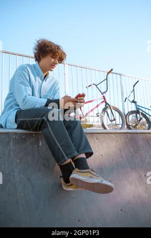 Maschio Bmx biker svaghi sulla rampa in skatepark dopo l'allenamento. Sport estremi in bicicletta, esercizi pericolosi in bicicletta, passeggiate in strada, escursioni in bicicletta nel parco estivo Foto Stock