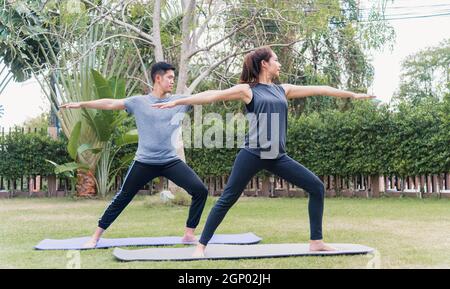 Giovane madre asiatica, padre che pratica gli esercizi di yoga con la figlia del bambino all'aperto in meditate ponga insieme nella natura un campo giardino parco, famil Foto Stock