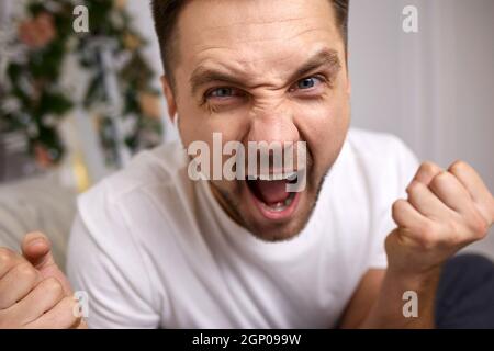 un giovane arrabbiato degli auricolari sta parlando con qualcuno in videochiamata. l'uomo urla Foto Stock