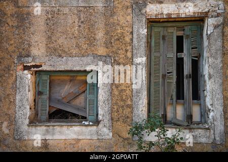Vecchia casa rurale abbandonata finestra con persiane di legno vecchio su un muro di pietra intemperie in Attica, grecia. Foto Stock