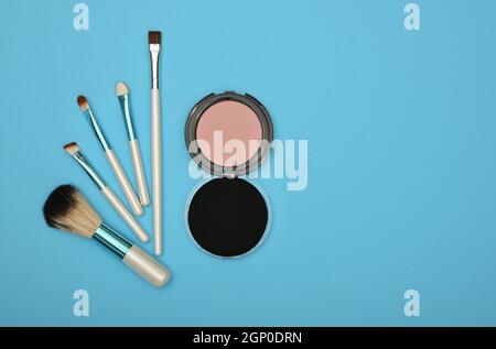 Primo piano set di trucco viso arrossito, spugna beige e pennelli su sfondo blu, vista dall'alto, direttamente sopra Foto Stock