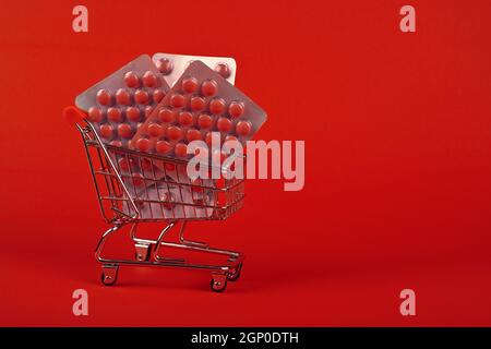 Primo piano diversi blister confezioni di pillole in piccolo carrello di shopping su sfondo rosso, concetto di online medicina ordine consegna, basso angolo vie Foto Stock