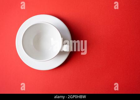 Semplice composizione piatta con tazza bianca in ceramica vuota, tazza, ciotola su un piatto con sfondo rosso brillante, vista dall'alto, spazio per il testo Foto Stock