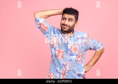 Profondo nei pensieri. Uomo confuso e pensivo con capelli scuri e barba in casual maglietta blu che graffia la testa, domandandosi e avendo dubbi, ponderando idea. Studio interno girato isolato su sfondo rosa. Foto Stock