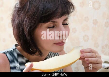 Una donna con un melone fragrante nelle mani chiuse gli occhi con piacere. Foto Stock