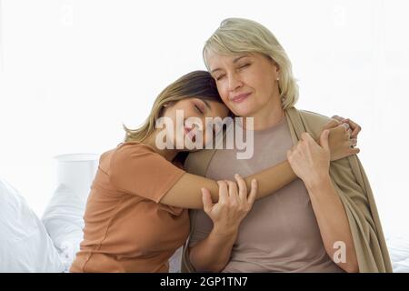 Happy mix pelle famiglia vivere insieme, figlia asiatica e adottato cuddle madre caucasica a vicenda con sorrisi. Concetto di amore e di condivisione del tempo Foto Stock