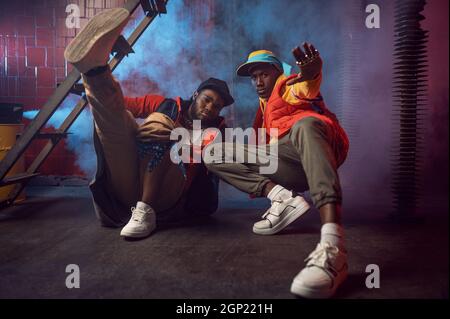 Due seri rapper con gioielli in oro pone in studio fresco, decorazione sotterranea. Artisti hip-hop, cantanti rap alla moda, ballerini break-dancer Foto Stock