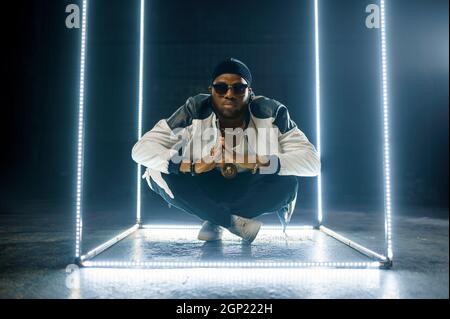 Elegante rapper in oro gioielli e occhiali da sole, sfondo scuro. Artista hip-hop, cantante rap, spettacolo di break-dance, stile di vita di intrattenimento Foto Stock
