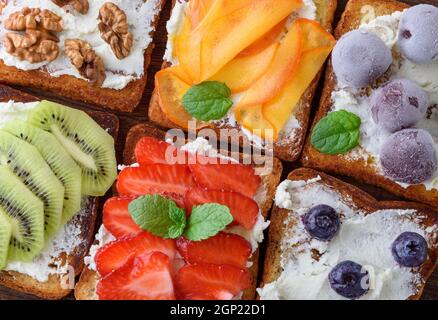 French Toast con formaggio a pasta morbida, fragole, kiwi, noci, ciliegie e mirtilli su un marrone di legno Foto Stock