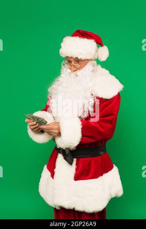Eccitato babbo natale che detiene dollari isolato sul verde Foto Stock